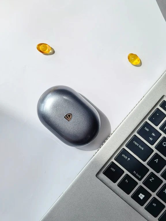 Top-down view of an oval SoundPEATS earphone charging case on a desk beside a laptop keyboard.