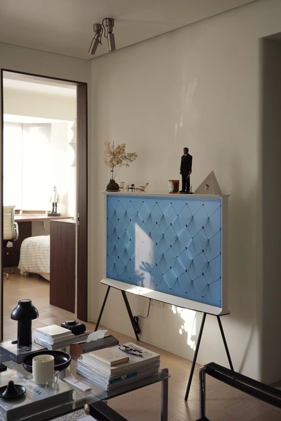 Modern designer television with floor tripod stand and light blue decorative screen panel in a bright living room