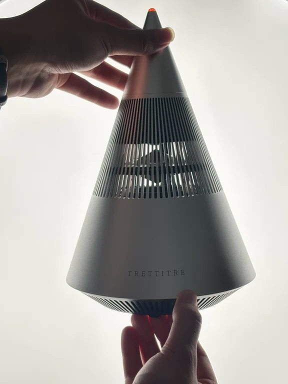 Silver cone-shaped Trettitre omnidirectional speaker held up with warm indicator light at the peak
