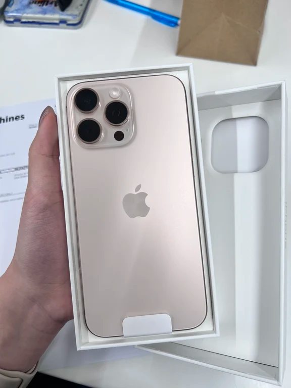 Gold or Desert Titanium iPhone Pro model resting in its open white retail box held by a hand