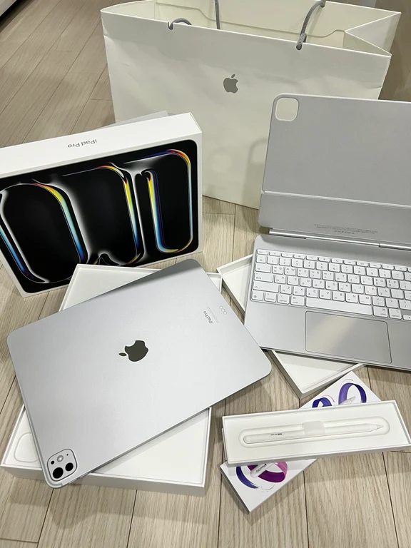 Unboxed silver iPad Pro alongside an Apple Magic Keyboard, Apple Pencil, and retail packaging.