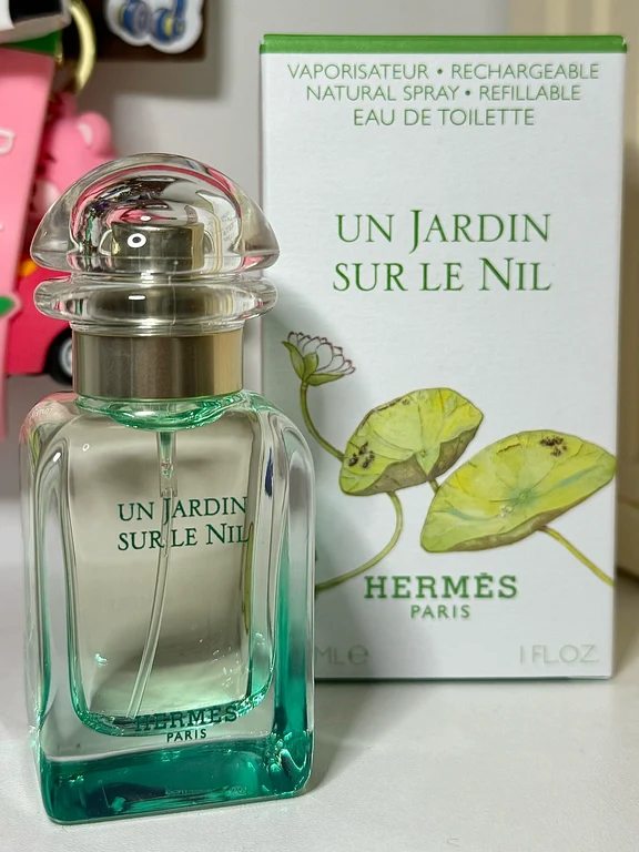 زجاجة عطر إيرميس أن جاردان سور لو نيل بجانب علبتها البيضاء المزينة برسومات اللوتس