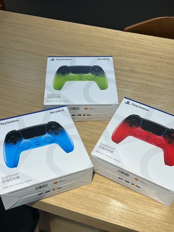 Three packaged PS5 DualSense controllers in green, blue, and red gradient boxes