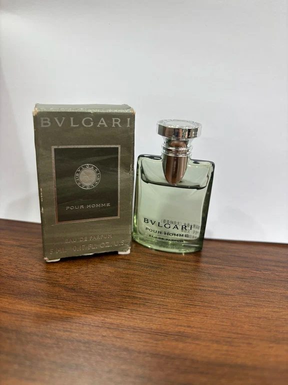 زجاجة عطر مصغرة من بولغاري بور هوم بجانب علبتها الكرتونية الخضراء