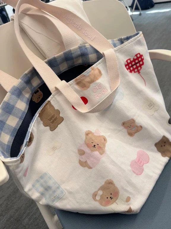 Open white canvas tote bag with printed teddy bears, red hearts, and blue gingham lining