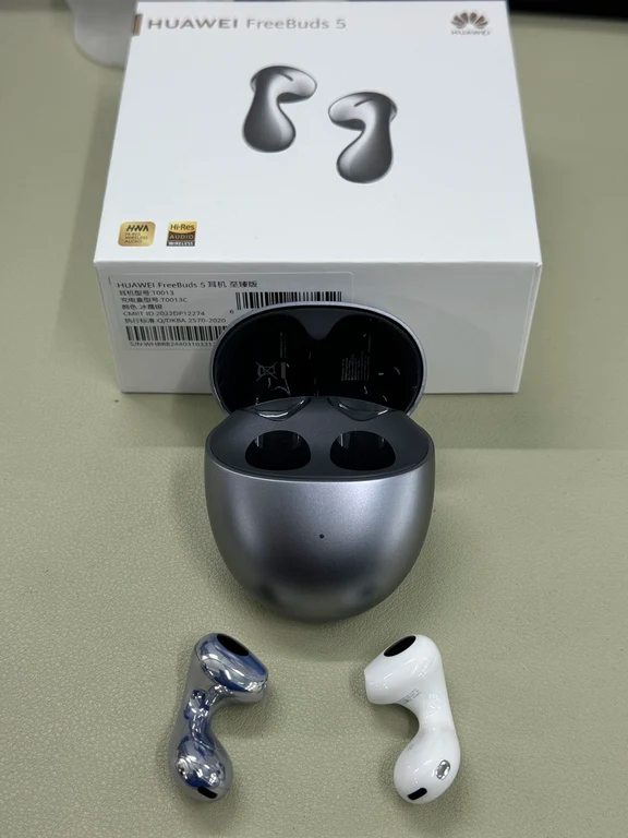 Huawei FreeBuds 5 packaging box, charging case, and droplet-style earbuds resting on a desk.