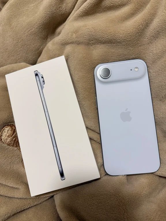 Back view of a light-colored smartphone with a single horizontal camera island beside its slim retail packaging box.