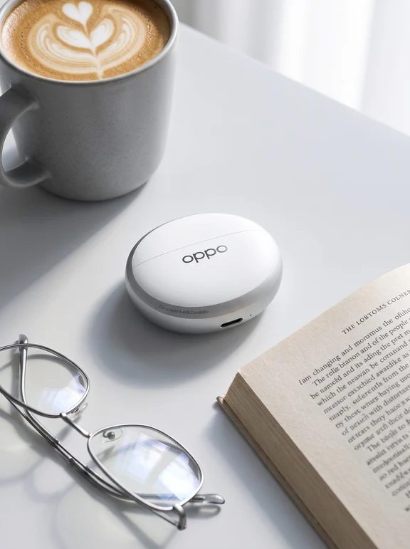 White oval Oppo earphone charging case on a white desk next to a latte and an open book