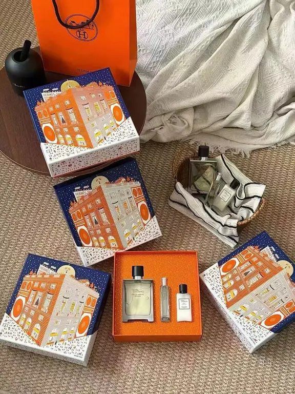 Multiple Terre d'Hermès orange gift boxes and matching shopping bag with decorative building illustrations arranged on carpet.