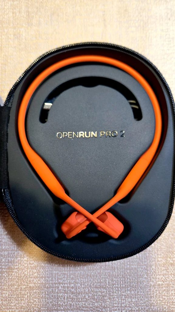 Orange open-ear neckband sports headset stored inside a black zippered case labeled OpenRun Pro 2