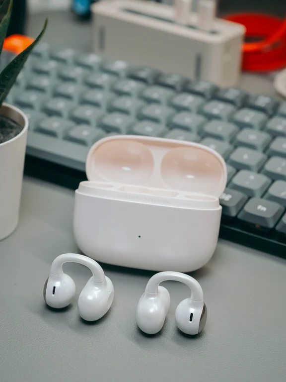 White clip-style wireless earphones resting on a desk in front of an open white case.