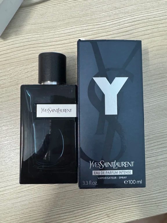 Yves Saint Laurent Y Eau de Parfum Intense 100ml perfume bottle and packaging box on a wooden desk.