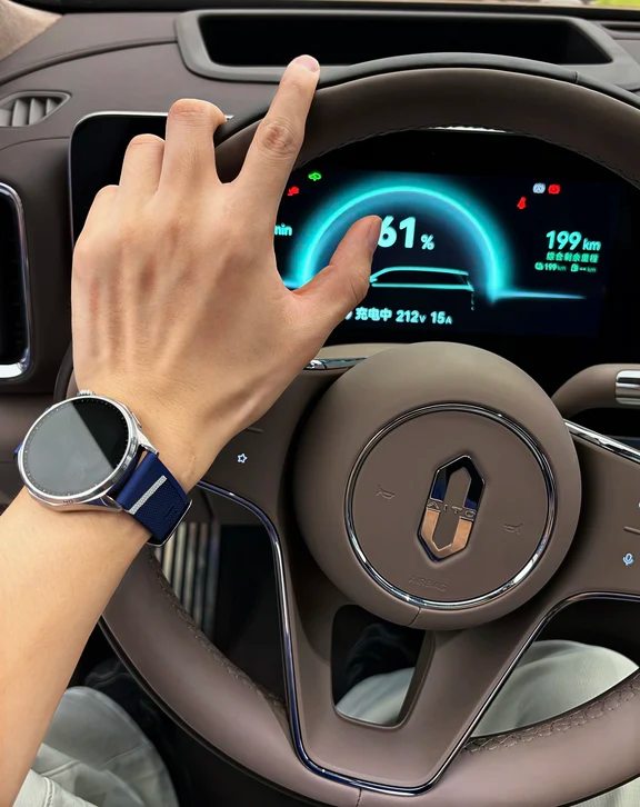 Smartwatch with a blue sports strap worn on a wrist resting on a modern car steering wheel