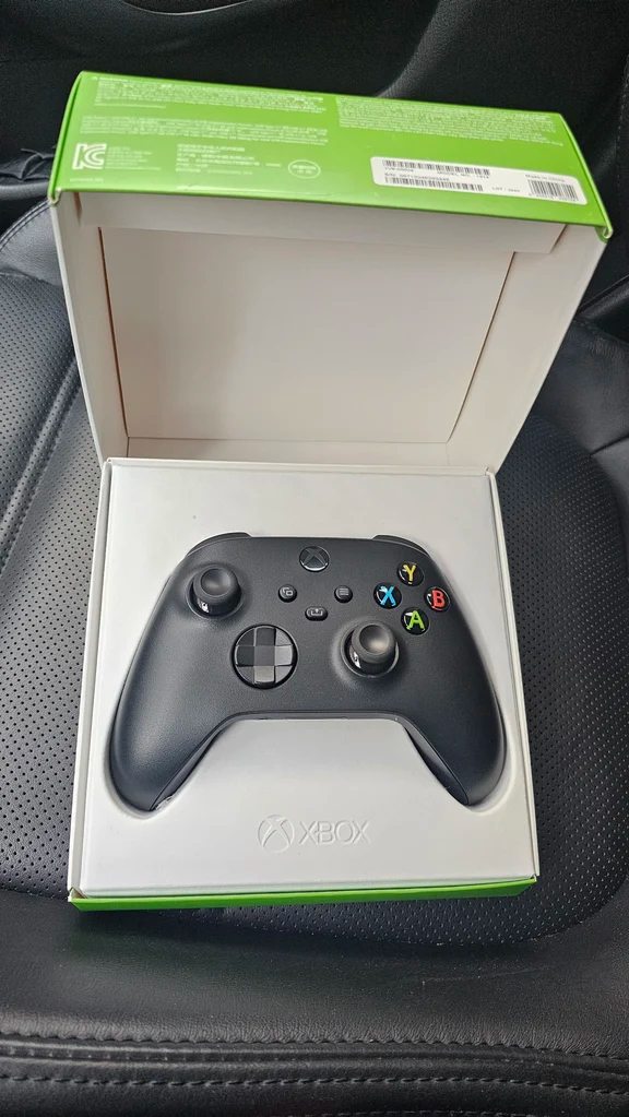 Black Xbox wireless controller resting in its open green retail box
