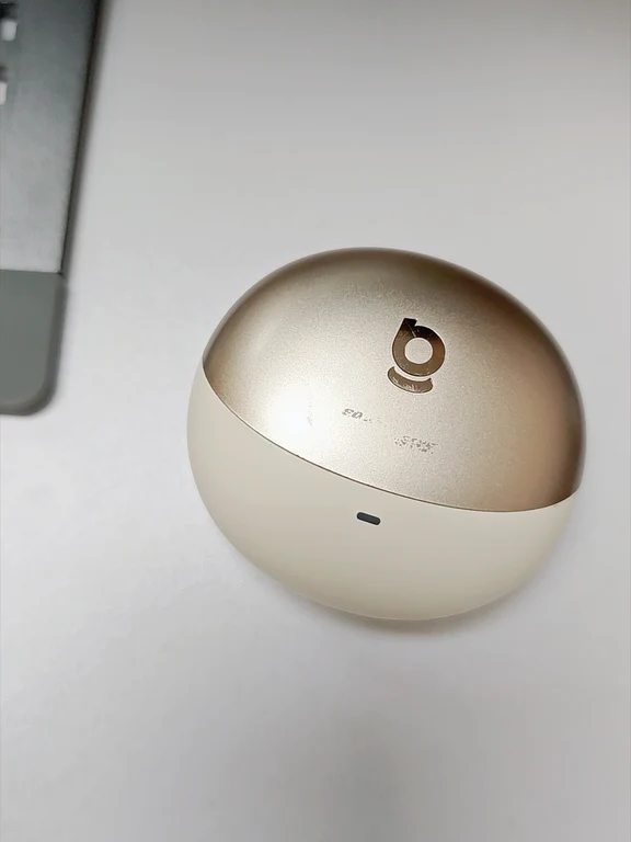 Pebble-shaped earphone charging case with a dual-tone gold and cream finish on a desk