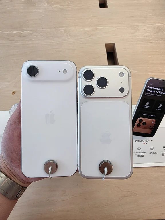 Hand displaying two white concept phones next to an in-store iPhone display stand
