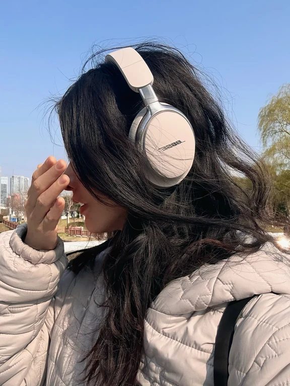 A young woman wearing cream-colored Bose over-ear headphones outdoors on a clear day.