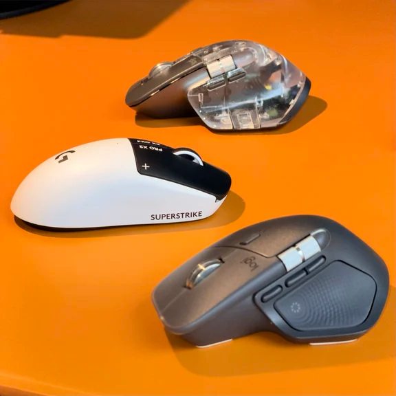 Three different computer mice on an orange surface including an ergonomic productivity mouse and gaming models
