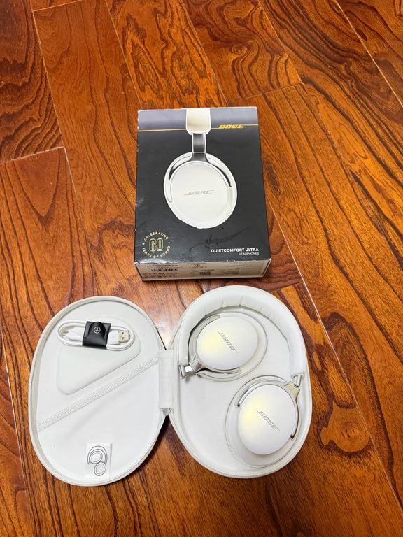 Retail packaging box for Bose QuietComfort Ultra headphones placed next to the opened case and USB cable on a wooden surface.