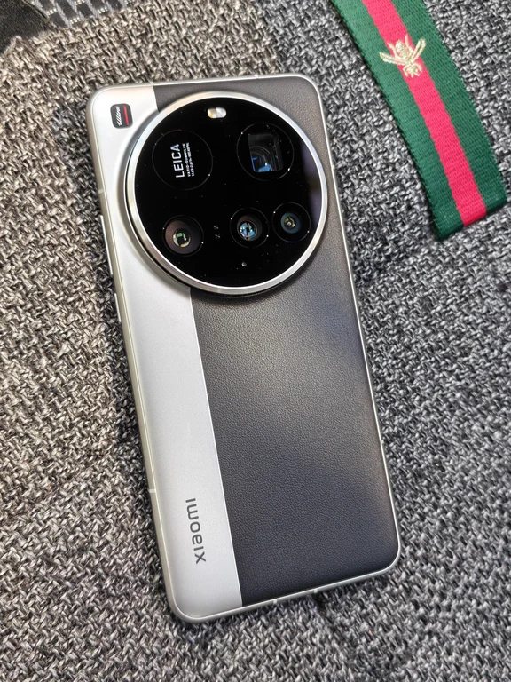 Silver and black smartphone with Leica circular quad-camera setup resting on textured grey fabric
