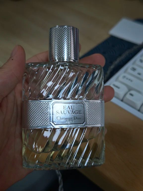 A hand holding a textured glass bottle of Christian Dior Eau Sauvage with silver cap.