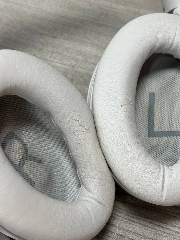 Macro close-up showing worn protein leather padding on the inner ring of white over-ear headphone cushions.