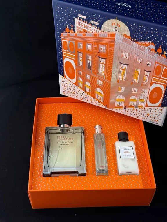 An opened orange Terre d'Hermès gift set showing the main perfume bottle, a slim travel spray, and an after-shave balm.