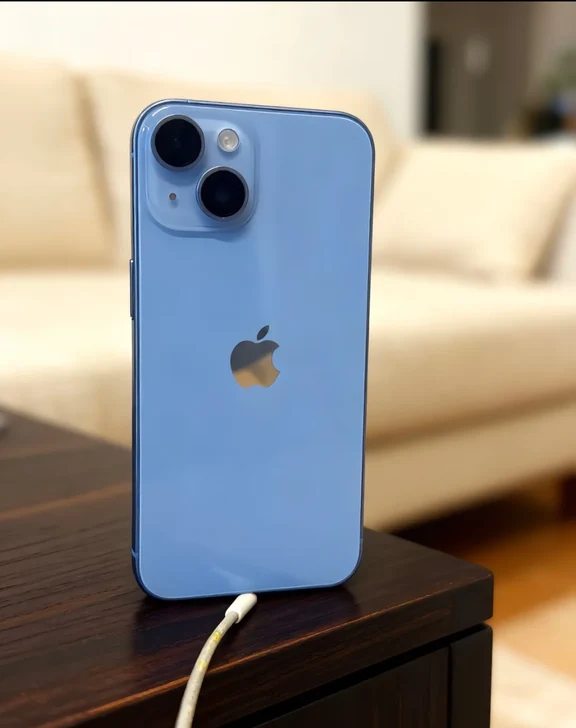 Back view of a light blue smartphone plugged into a white charging cable on a wooden tabletop
