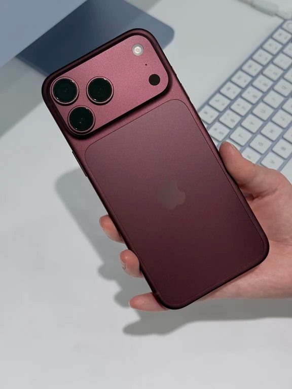 Hand holding a deep burgundy red smartphone with three rear camera lenses in a horizontal housing
