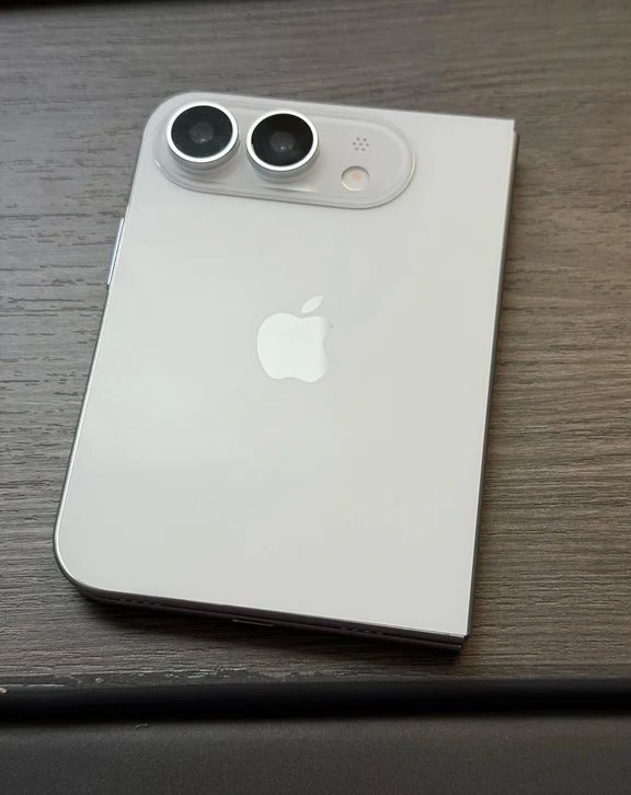 White foldable iPhone concept shown in folded state with horizontal dual-lens camera island on a wood surface