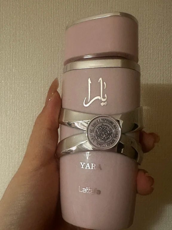 Hand holding a pale pink 100ml Lattafa Yara Eau de Parfum bottle with silver crisscross accents.