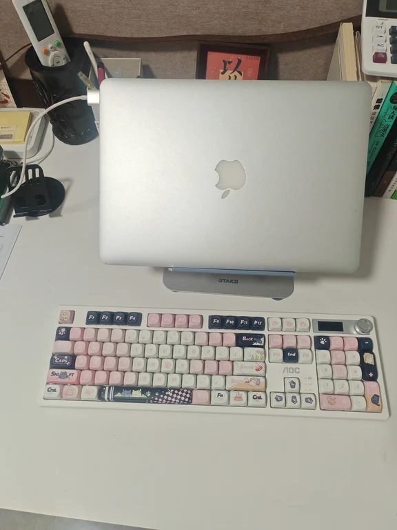 White desk keyboard with cute pastel pink and decorative keycaps in front of a laptop