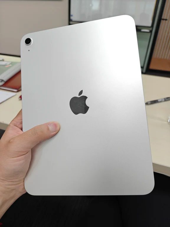 Hand holding a silver Apple iPad tablet showing the rear metal casing and camera module