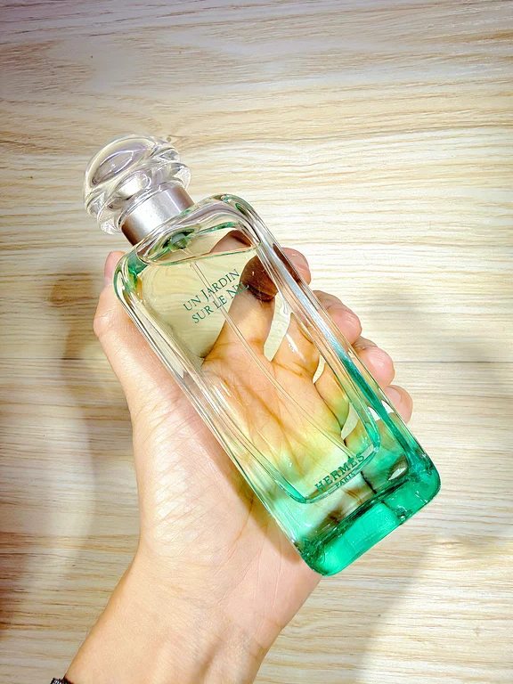 يد تمسك بزجاجة عطر إيرميس أن جاردان سور لو نيل ذات القاعدة الخضراء المتدرجة