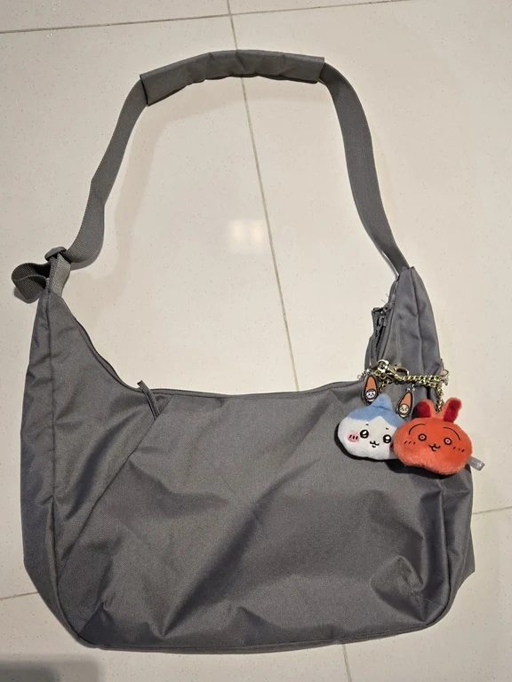 Dark grey nylon crescent shoulder bag lying flat on floor with two cute plush charms