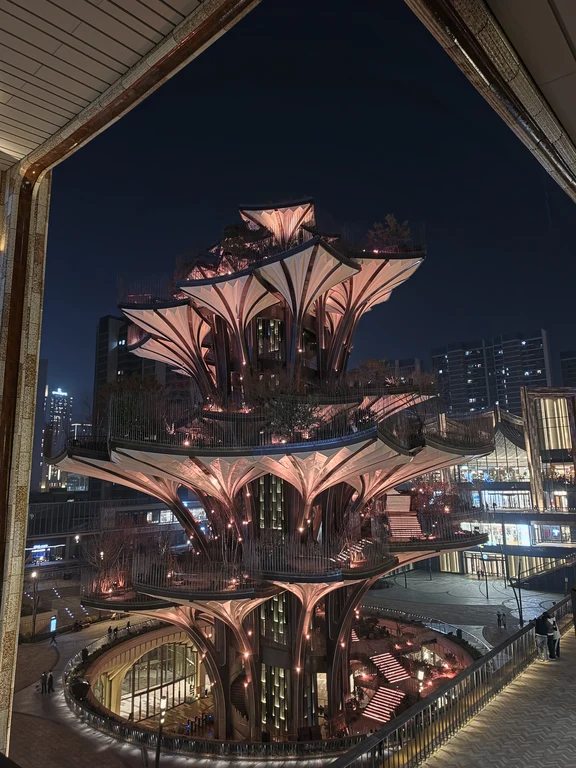 Illuminated multi-tiered architectural outdoor pavilion captured at night from an elevated angle