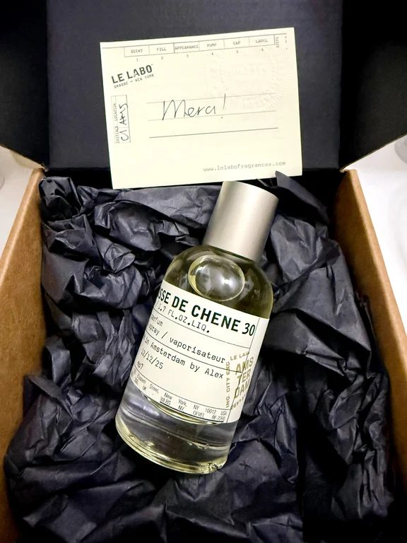 A bottle of Le Labo Mousse de Chene 30 Eau de Parfum resting inside a cardboard box with black tissue paper and a handwritten note.