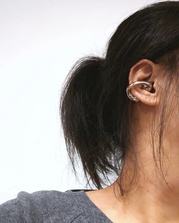 Profile view showing an ear-clip wireless earphone fitted comfortably around a user's outer ear.