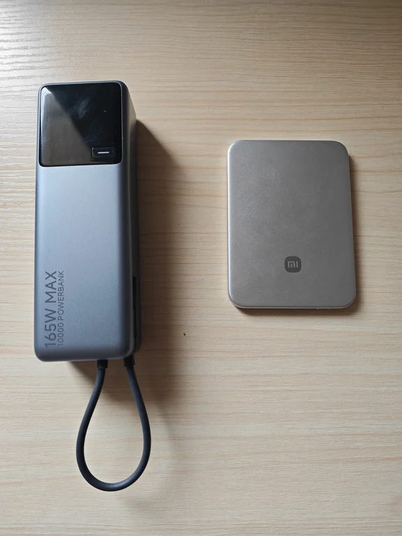 A tall gray 165W 10000mAh power bank with an integrated loop cable next to a compact silver Xiaomi power bank on a wooden surface.