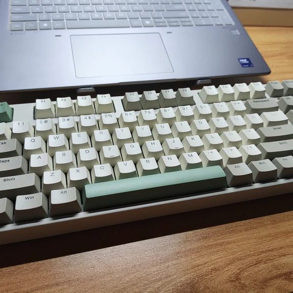 Mechanical keyboard with sage green and off-white keycaps placed before a laptop