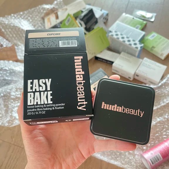 Huda Beauty Easy Bake loose baking powder packaging box next to a black square powder container