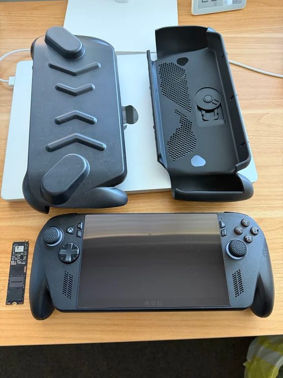 Black ROG Ally handheld console lying next to protective case covers and an SSD drive