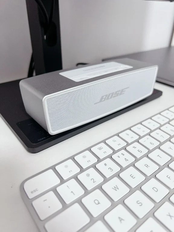 Silver Bose SoundLink Mini II speaker with front metal grille resting on a desk next to a white keyboard.