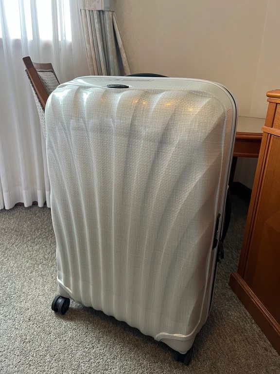 Close-up of a pearl white Samsonite shell textured suitcase standing on carpet near wooden furniture