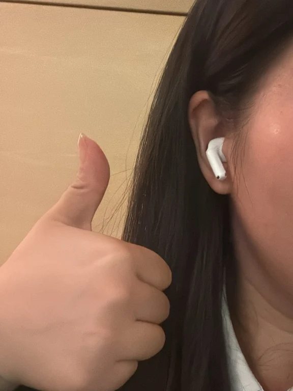 Person wearing a white semi-in-ear wireless earbud and giving a thumbs up