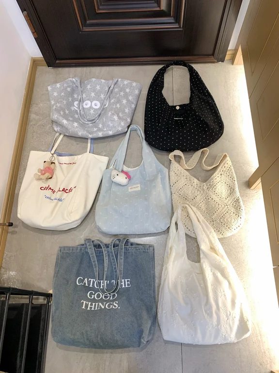Arrangement of seven fabric and denim shoulder bags and totes on a floor