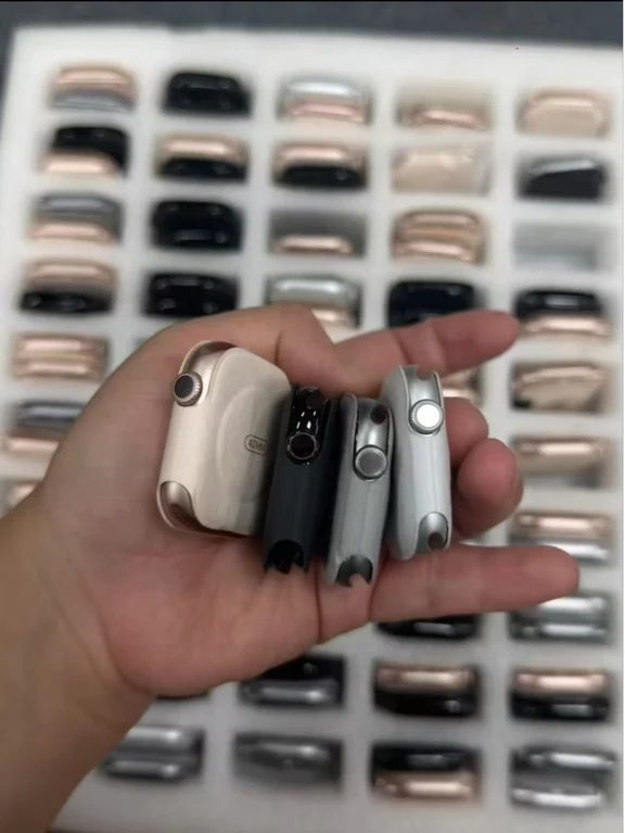 A hand holding several Apple Watch cases displaying different side profiles, colors, and button layouts
