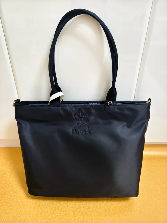 Black nylon tote bag with top shoulder straps and subtle embroidered text