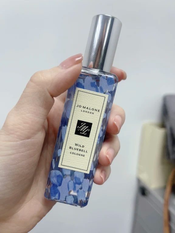 يد تحمل زجاجة عطر جو مالون وايلد بلو بيل بحجم صغير مع زخرفة زرقاء مزهرة