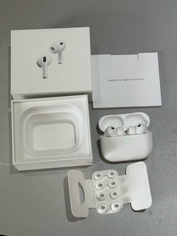 Unboxed white Apple AirPods Pro charging case, retail box, paperwork, and multiple sizes of replacement silicone ear tips